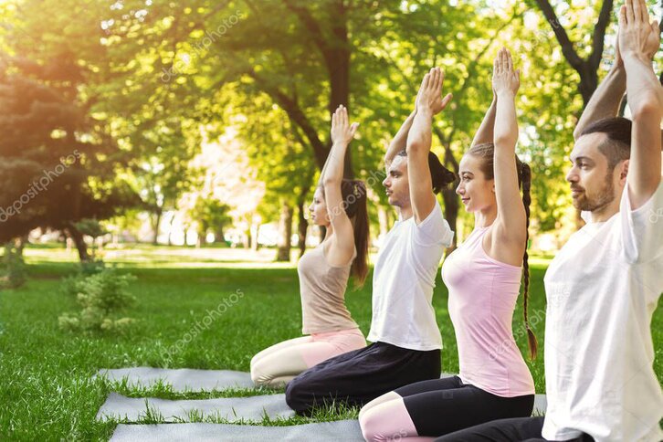 Persone sedute sull’erba che partecipano a un’attività di benessere nel parco